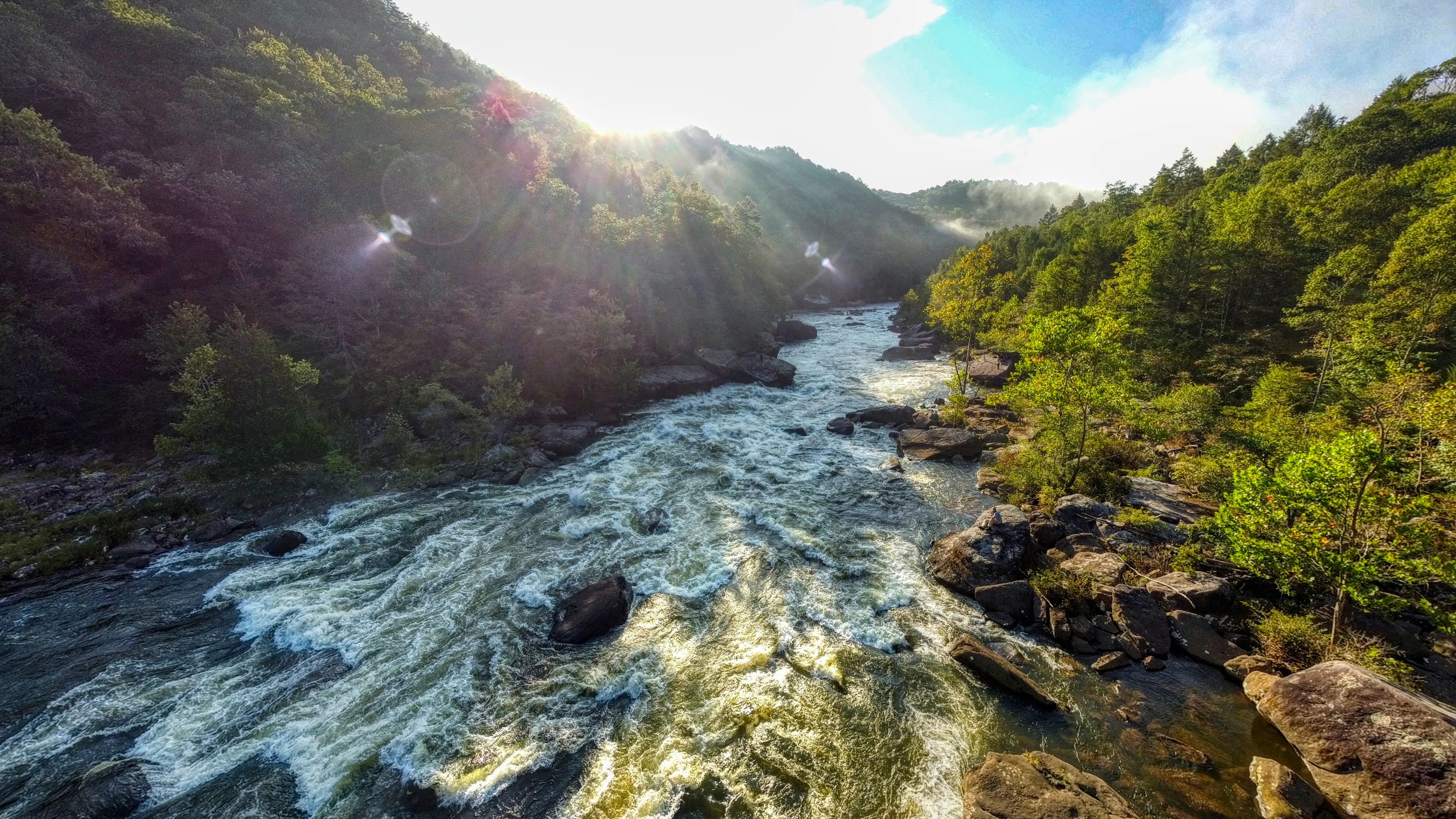 Morning sun breaking over forested mountains above the rapids of the Gauley River