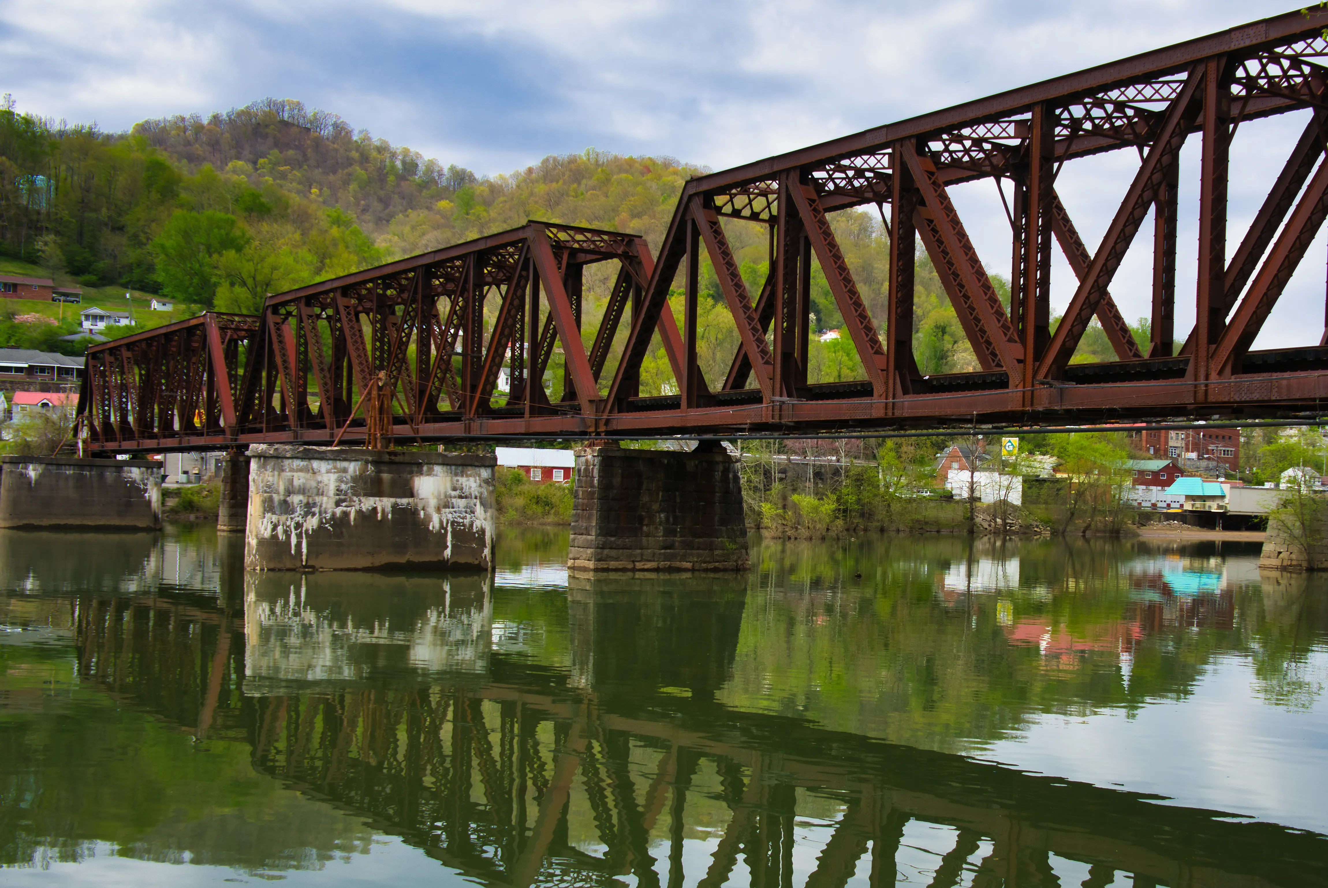 Steel railroad truss bridge spanning a calm green river in a West Virginia town